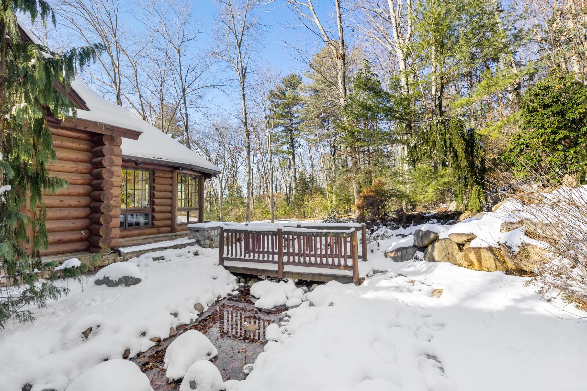 The timber footbridge crossing the snow-banked stream to The Lodge