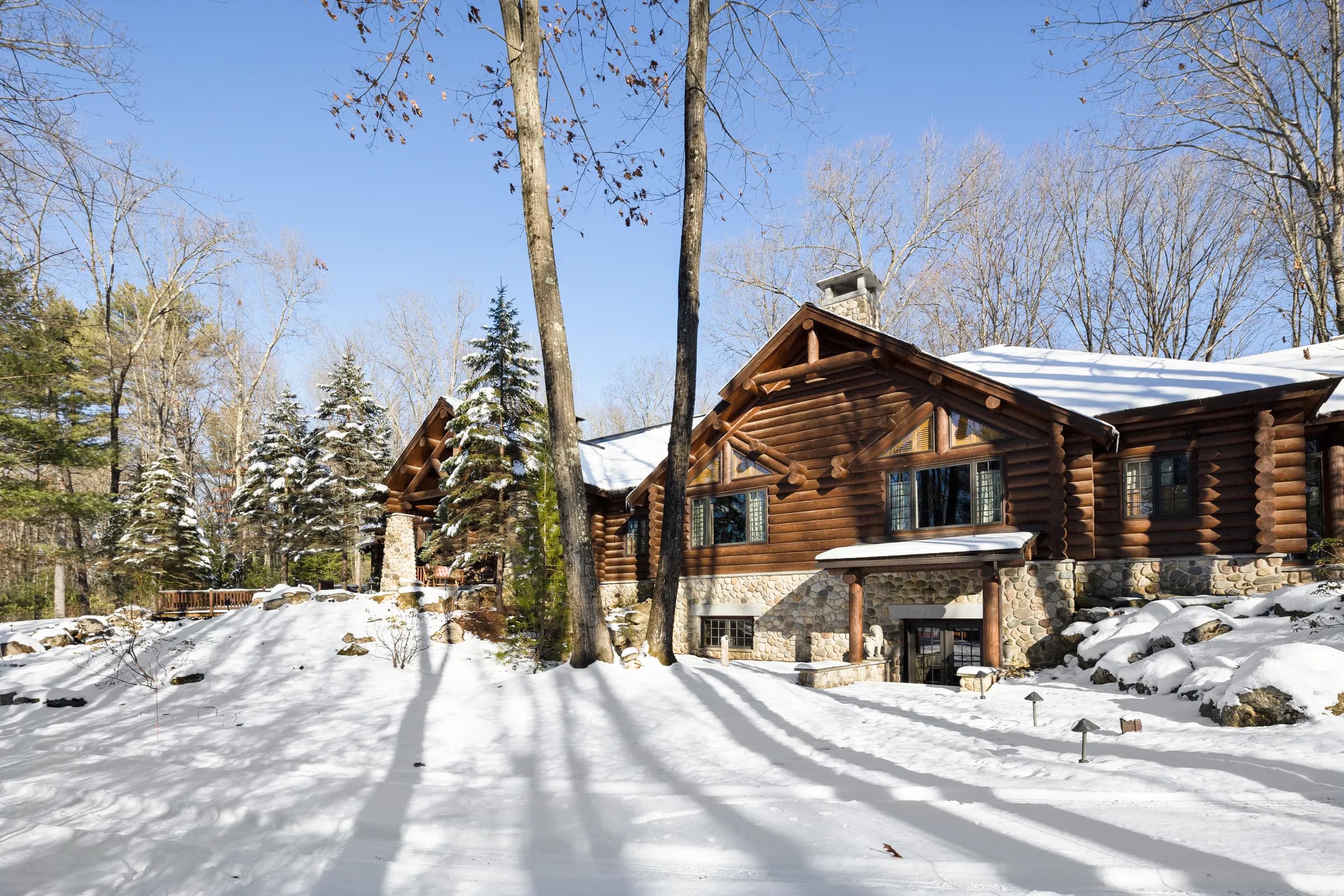 The hand-hewn log facade and stone chimneys of The Lodge under winter sun