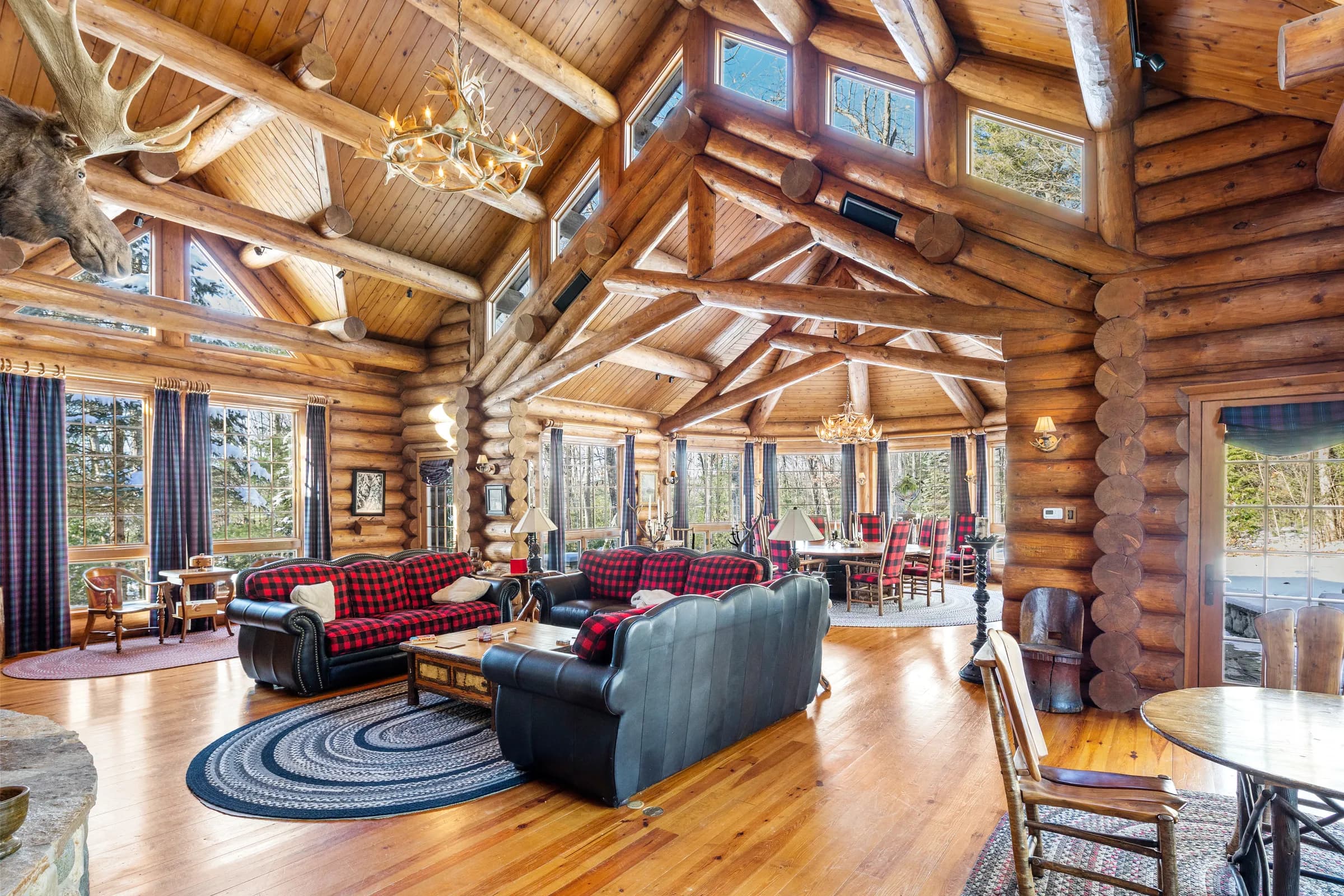 The great room's log trusses and antler chandelier over buffalo-plaid and leather sofas
