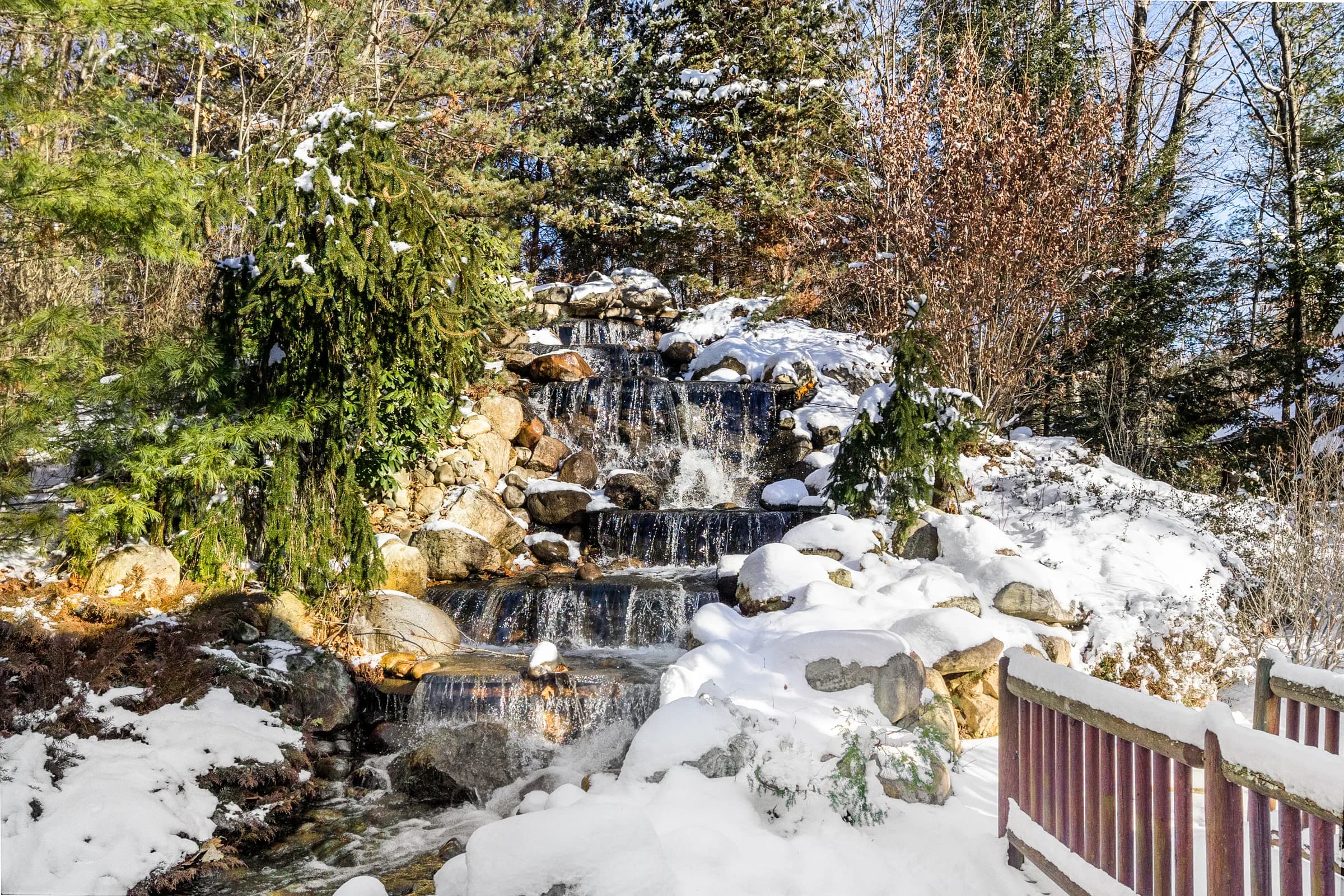 The Lodge's waterfall cascading over snow-covered boulders beside the timber footbridge